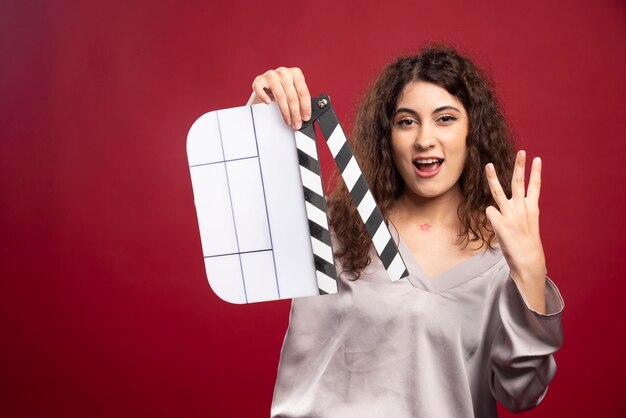 Brunette woman with clapperboard showing her hand.