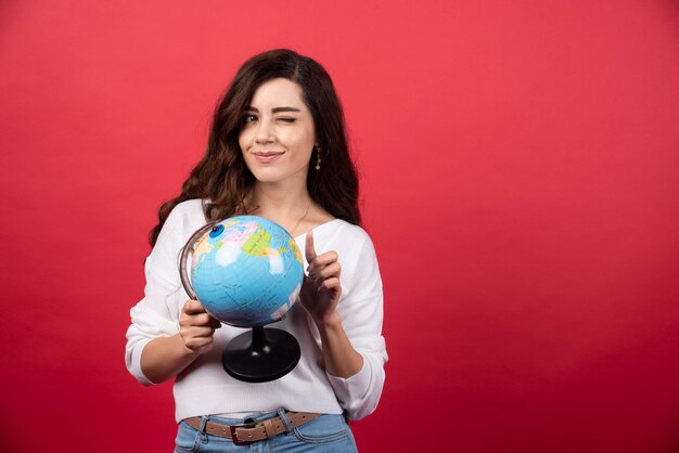 Brunette woman with globe closing her one eye. High quality photo