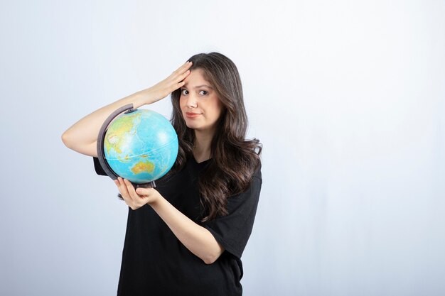 Brunette woman with long hair holding world globe and posing . 
