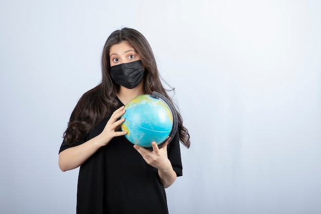 Brunette woman with long hair in medical mask holding world globe . 