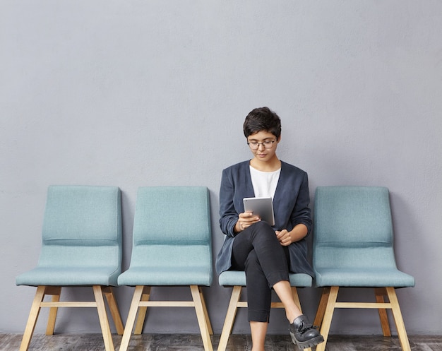 Brunette young woman sitting on chair and holding tablet