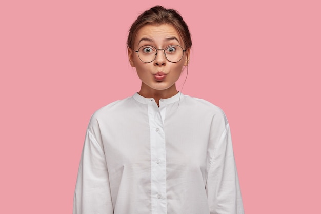 Free photo brunette young woman with glasses posing against the pink wall