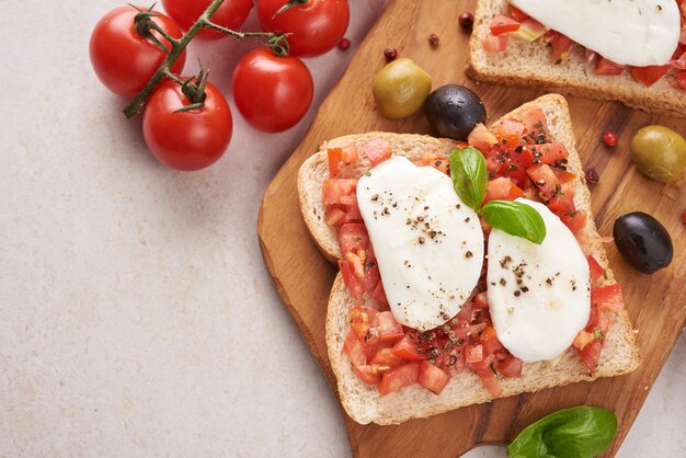 Bruschetta with tomatoes, mozzarella cheese and basil on a cutting board. Traditional italian appetizer or snack, antipasto. Caprese salad bruschetta. Top view with copy space. Flat lay.