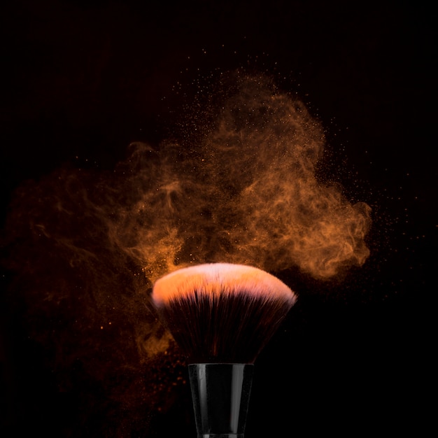 Free photo brush for makeup in powder burst on dark background