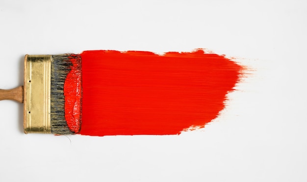 Brush with red paint lies on a white surface, top view, paint samples before work, choice of paints