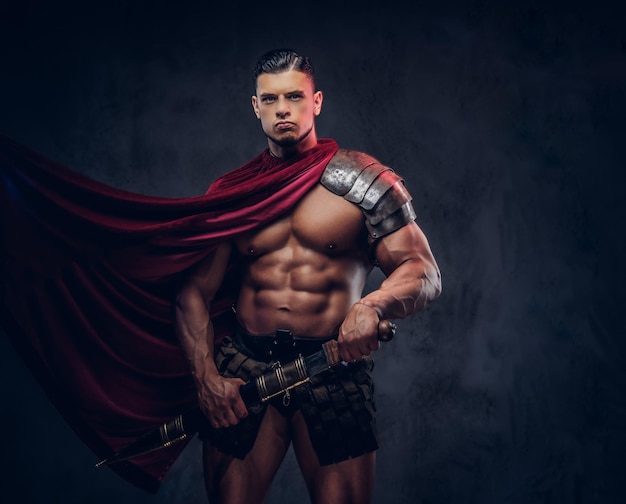 Brutal ancient Greece warrior with a muscular body in battle uniforms posing on a dark background.