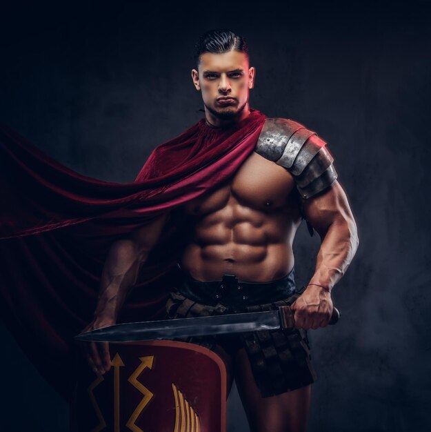 Brutal ancient Greece warrior with a muscular body in battle uniforms posing on a dark background.