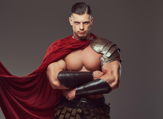 Brutal ancient Greece warrior with a muscular body in battle uniforms standing with crossed arms. Isolated on a gray background.