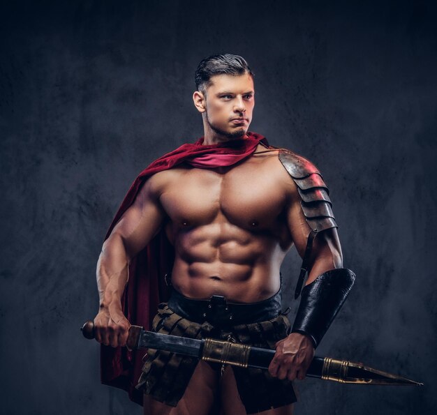 brutal ancient greek warrior with a muscular body in battle equipment posing on a dark background.