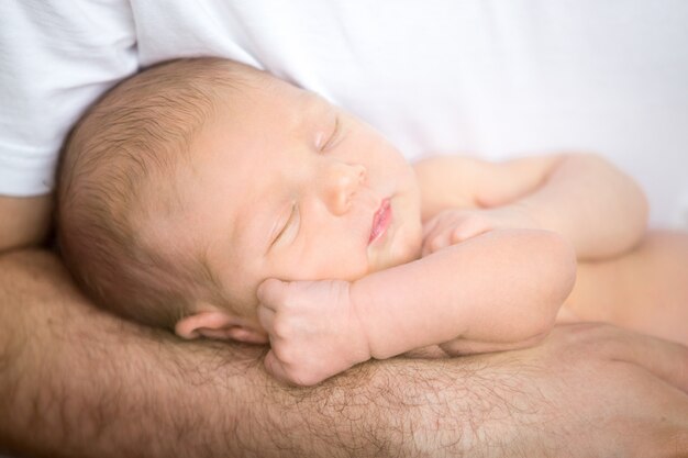 眠っている新生児を持っている残忍な男性の手