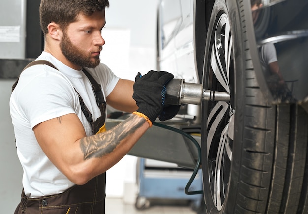 Brutal mechanic fixing hubcap of car wheel.