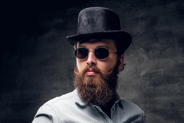 Brutal modern man in retro sunglasses and hat is posing at photo studio.