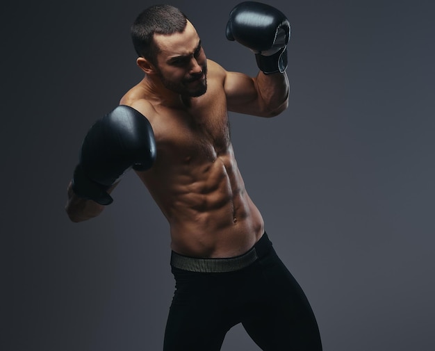 Жестокий кавказский спортсмен без рубашки в боксёрских перчатках тренируется изолированно на сером фоне.