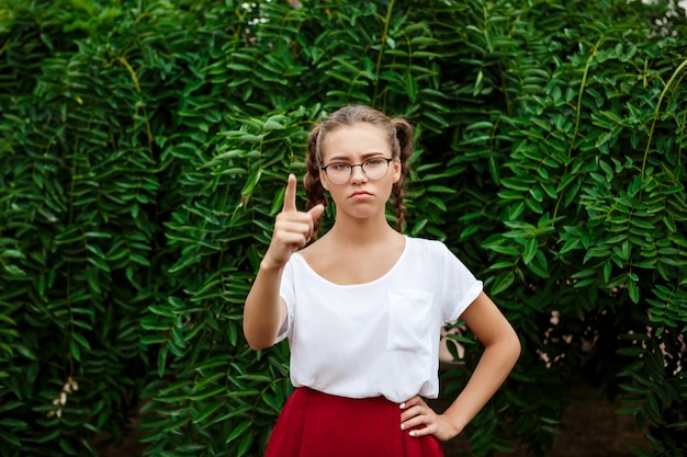 Brutal young female student in glasses pointing finger at front