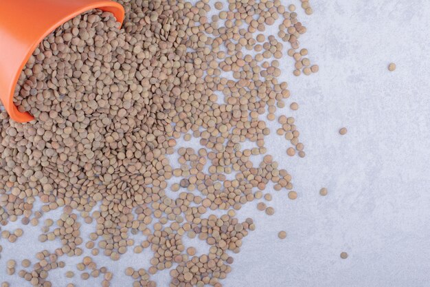 Bucket of brown lentil spilled all over marble surface