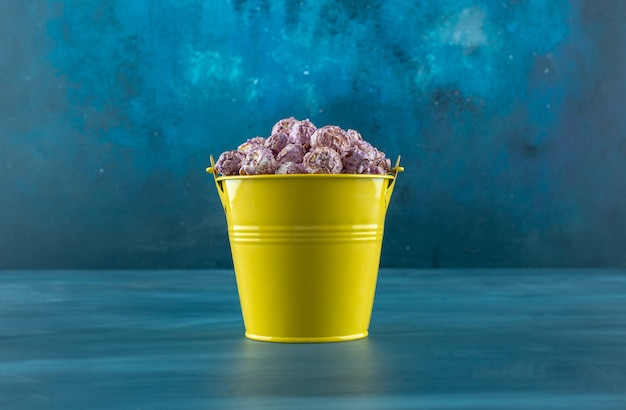Bucket of crunchy purple popcorn candy on blue background. High quality photo