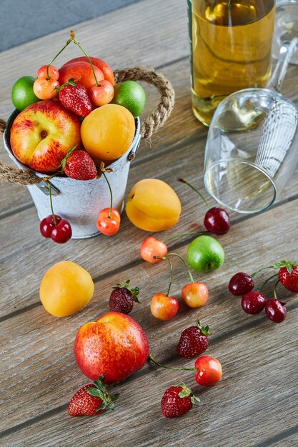 Bucket of fresh summer fruits, bottle of white wine and empty glass on wooden table.