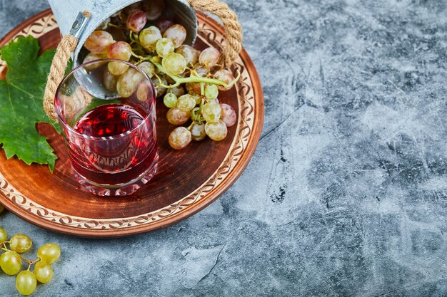 Bucket of of grapes and a glass of juice on marble.