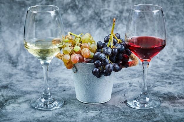 Bucket of grapes and glasses of wine on marble background