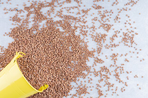 Bucket lying on a messy pile of buckwheat groats on marble surface