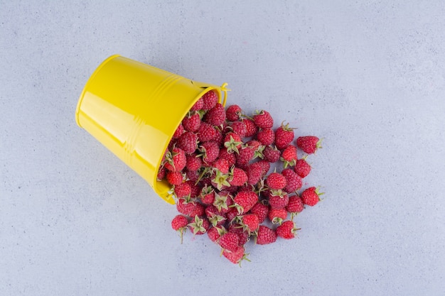 Bucket of raspberries spilled over on marble background.