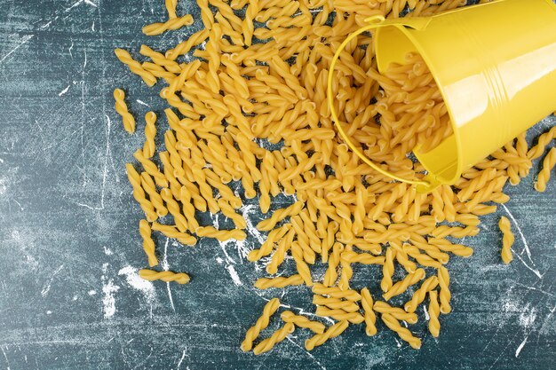 Bucket of raw spiral pasta scattered on blue background. High quality photo