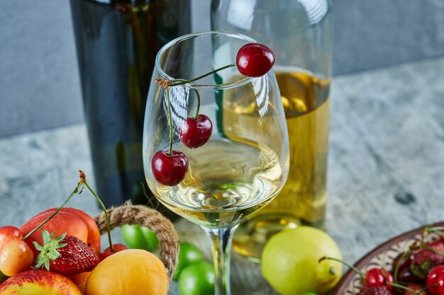 Bucket of summer fruits, lemon and a glass of white wine on marble surface