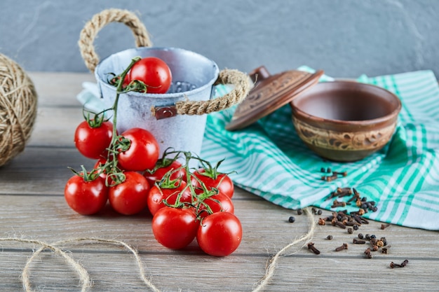 Bucket of tomatoes and cloves on wooden table with empty bowl