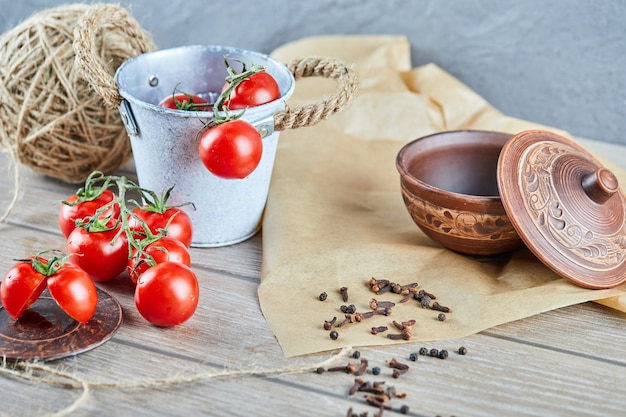 Bucket of tomatoes and half cut tomato on wooden table with empty bowl