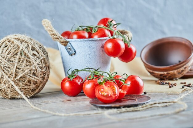 Bucket of tomatoes and half cut tomato on wooden table.