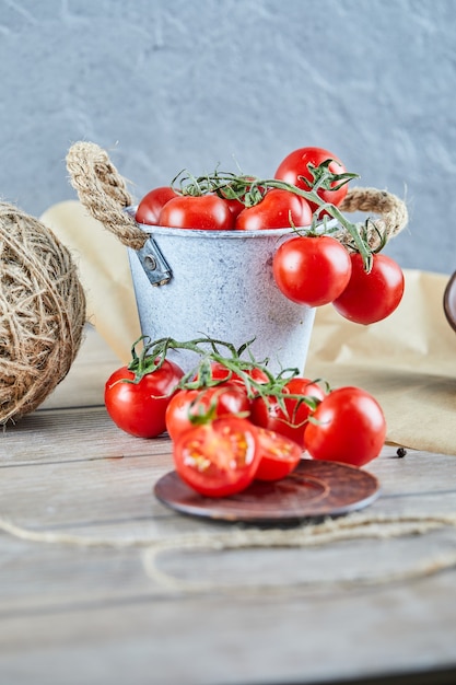 Bucket of tomatoes and half cut tomato on wooden table.