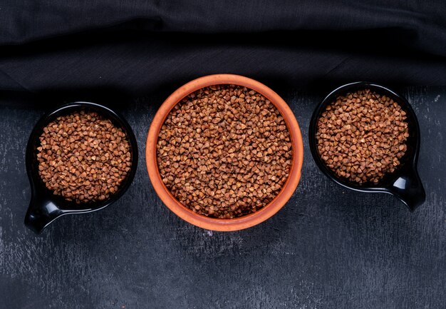 Buckwheat in a bowl and black cups on a dark . top view.