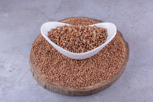 Buckwheat grains spread out on a wooden board around a bowl of cooked buckwheat on marble background. High quality photo