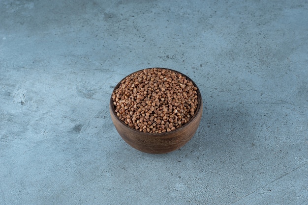 Buckwheat grains in a wooden cup on blue background. High quality photo