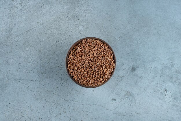 Buckwheat grains in a wooden cup on blue background. High quality photo