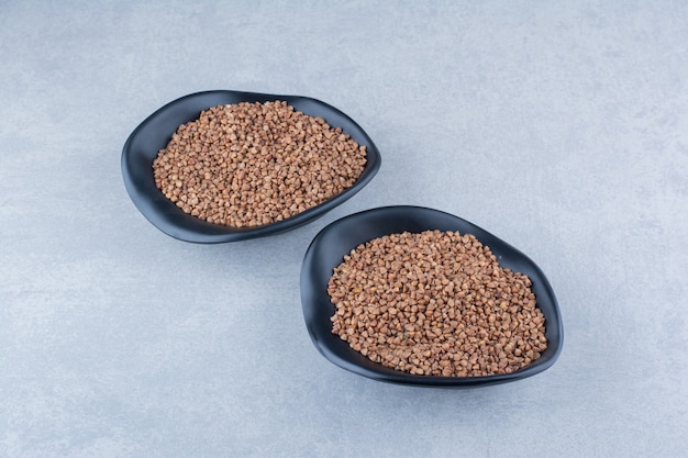 Free photo buckwheat groats piled in two bowls on marble background.