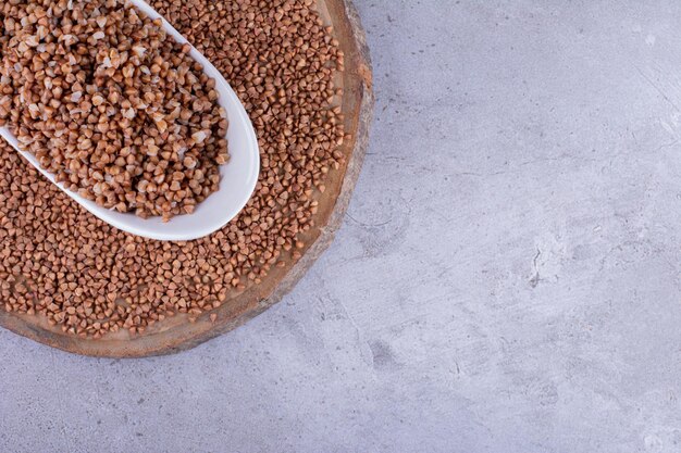 Buckwheat inside and surrounding a small bowl on a wooden tray on marble background. High quality photo