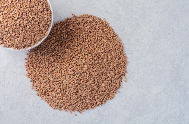 Buckwheat piled in a bowl and on marble surface