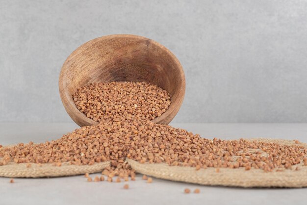 Buckwheat scattered all over trivets from a wooden bowl on marble table.