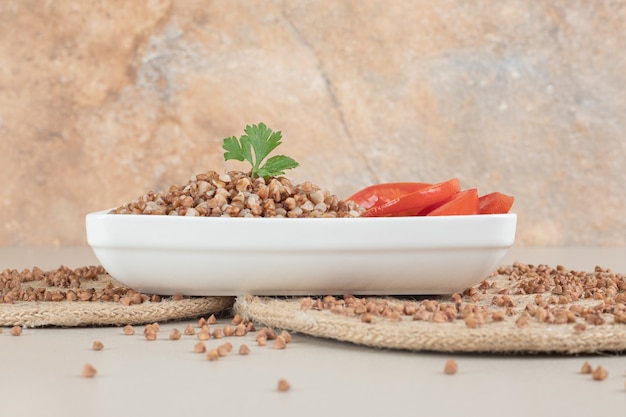 Semi di grano saraceno serviti con pianta verde e fette di pomodoro.