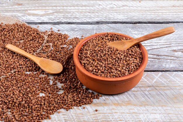 Buckwheats in a bowl and around with spoons high angle view on a light wooden 