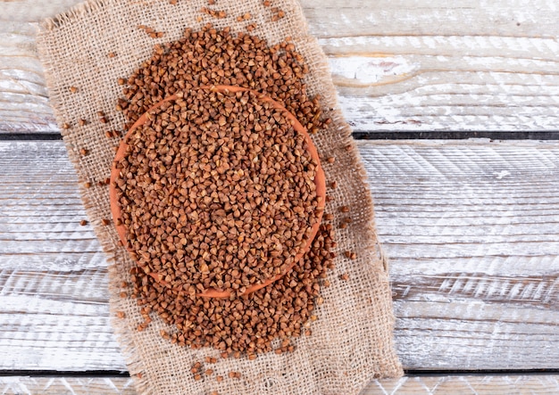 Buckwheats in a bowl on a sack cloth and light wooden . top view.