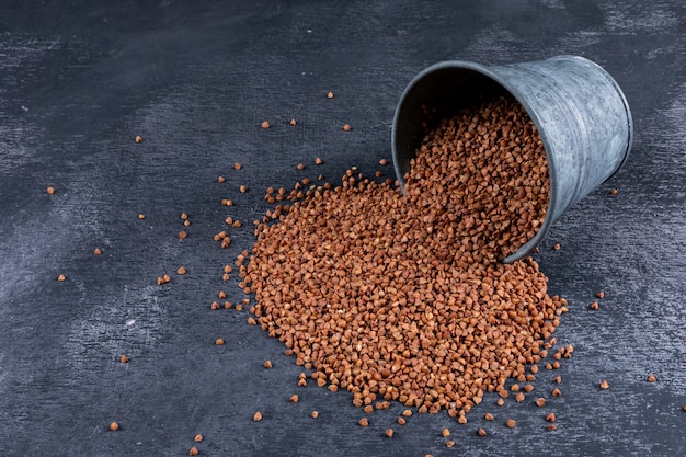 Buckwheats coming out of bucket on dark , high angle view.