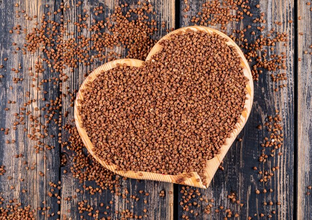 Buckwheats in a heart shaped cutting board on a dark wooden . top view.