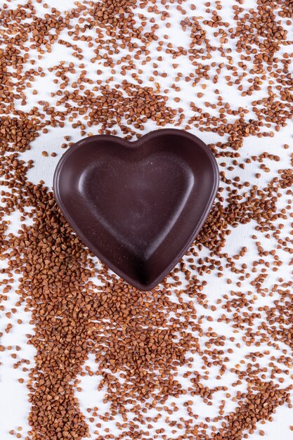 Free photo buckwheats with heart shaped empty bowl top view on a white