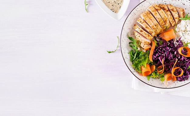 Buddha bowl dish with chicken fillet, rice,  red cabbage, carrot, fresh lettuce salad and sesame.