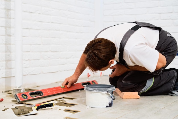 Builder checks the quality of the laid tiles with a manual bubble level construction worker installing ceramic floor tiles on construction sites floor repair selective focus