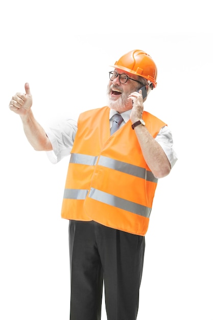 The builder in a construction vest and an orange helmet talking on a mobile phone about something