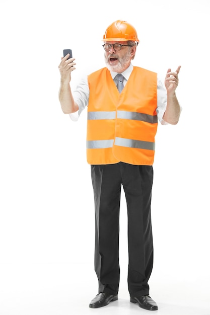 The builder in a construction vest and an orange helmet talking on a mobile phone about something.