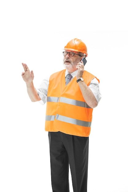 The builder in a construction vest and an orange helmet talking on a mobile phone about something